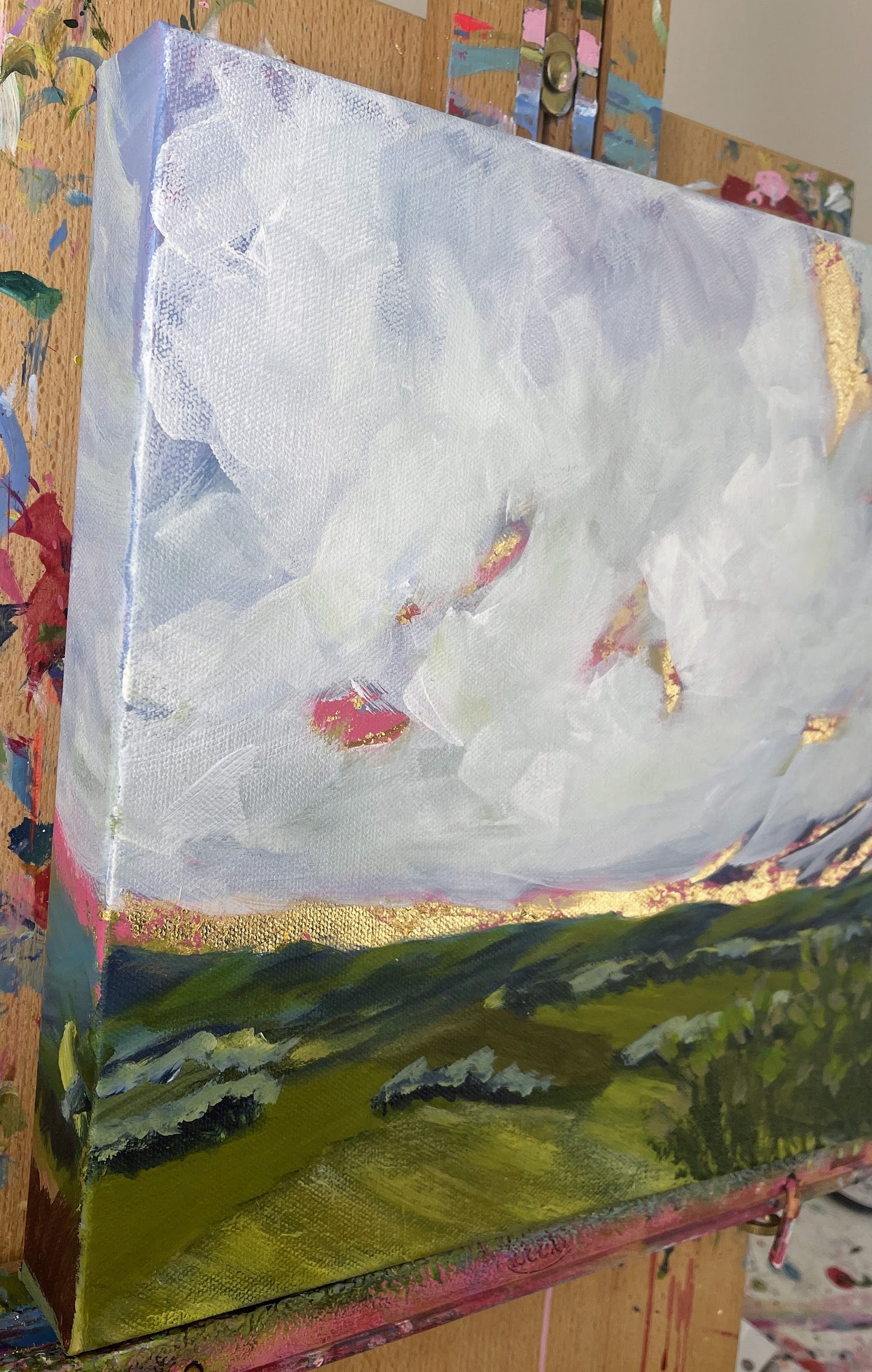painting of a landscape with clouds and green fields on a textured surface.