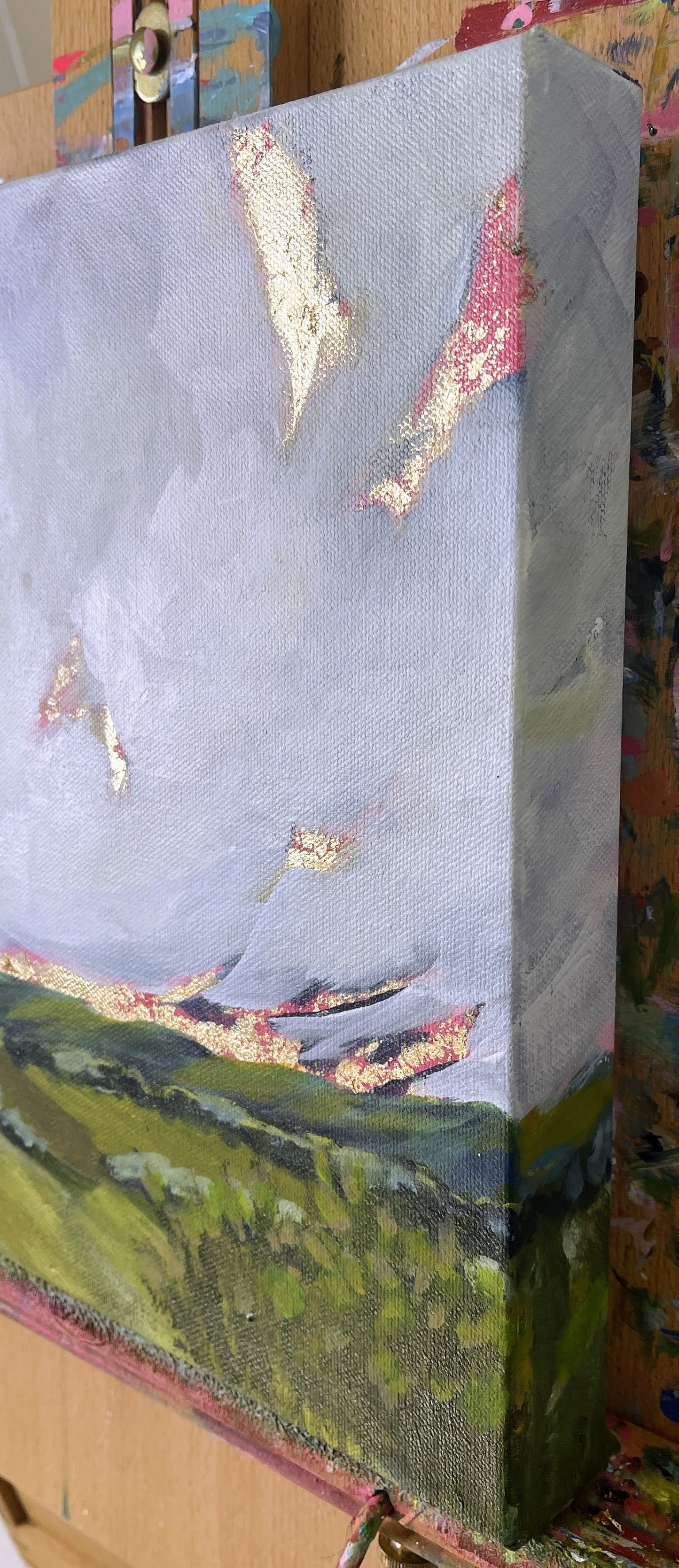 Partial view of a landscape painting with mountains and trees on an easel.