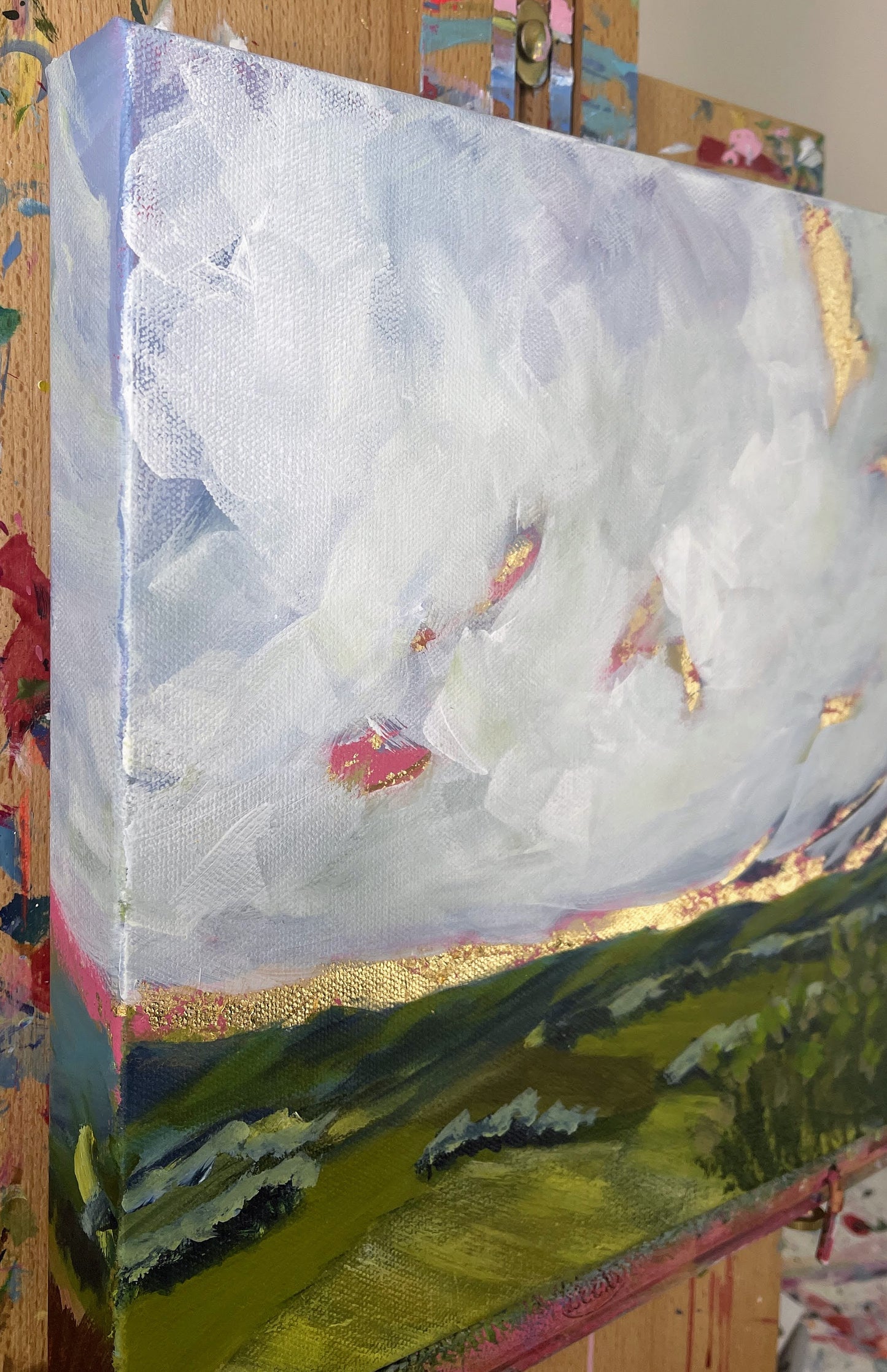 Canvas painting of a landscape with clouds and greenery on an easel.