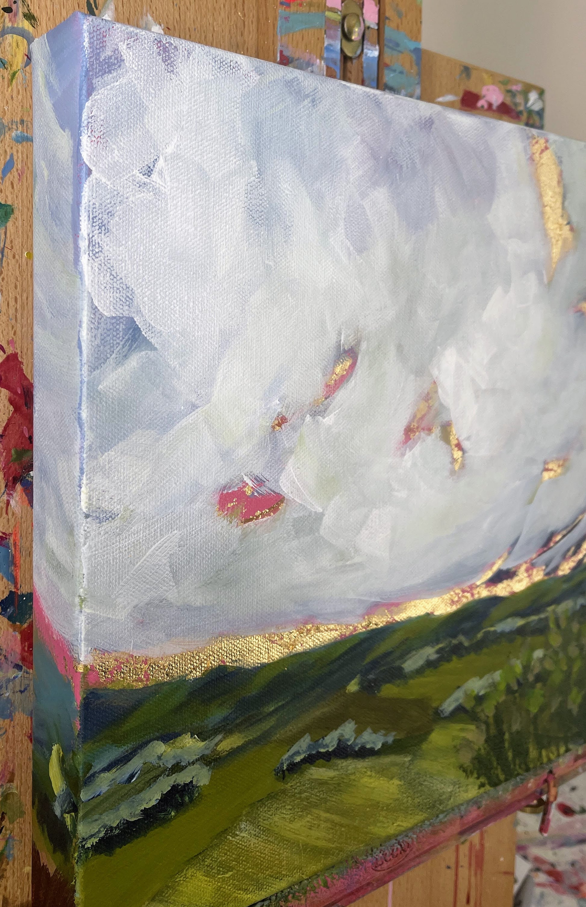 Canvas painting of a landscape with clouds and greenery on an easel.